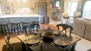 A dining area with a table set for six, kitchen cabinets, a refrigerator, and a living area with a sofa and a TV. - Friendly Nabors (Ruidoso)