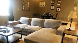 A living room with a sectional sofa, two coffee tables, a lamp, and framed pictures on the wall. - Friendly Nabors (Ruidoso)