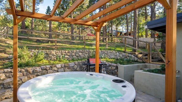 A hot tub under a wooden pergola in a landscaped outdoor area. - Friendly Nabors (Ruidoso)