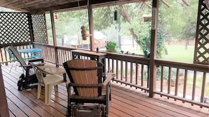 Eine überdachte Veranda mit Holzboden, einem Holzstuhl, einem Plastiktisch und einem Metallgrill.