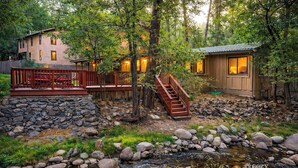 Une cabane avec un mur de soutènement en pierre, une terrasse en bois et un petit ruisseau.