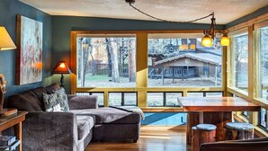 Un salon confortable avec un canapé, une table et une vue sur une maison, visible à travers de grandes fenêtres.