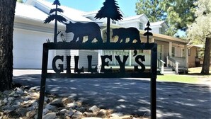 Une enseigne métallique portant l’inscription « GILLEY’S » et représentant des silhouettes d’ours, placée devant une maison avec un garage.