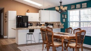 Une cuisine avec des meubles blancs, un réfrigérateur noir, un îlot central en bois et une table à manger avec des chaises.