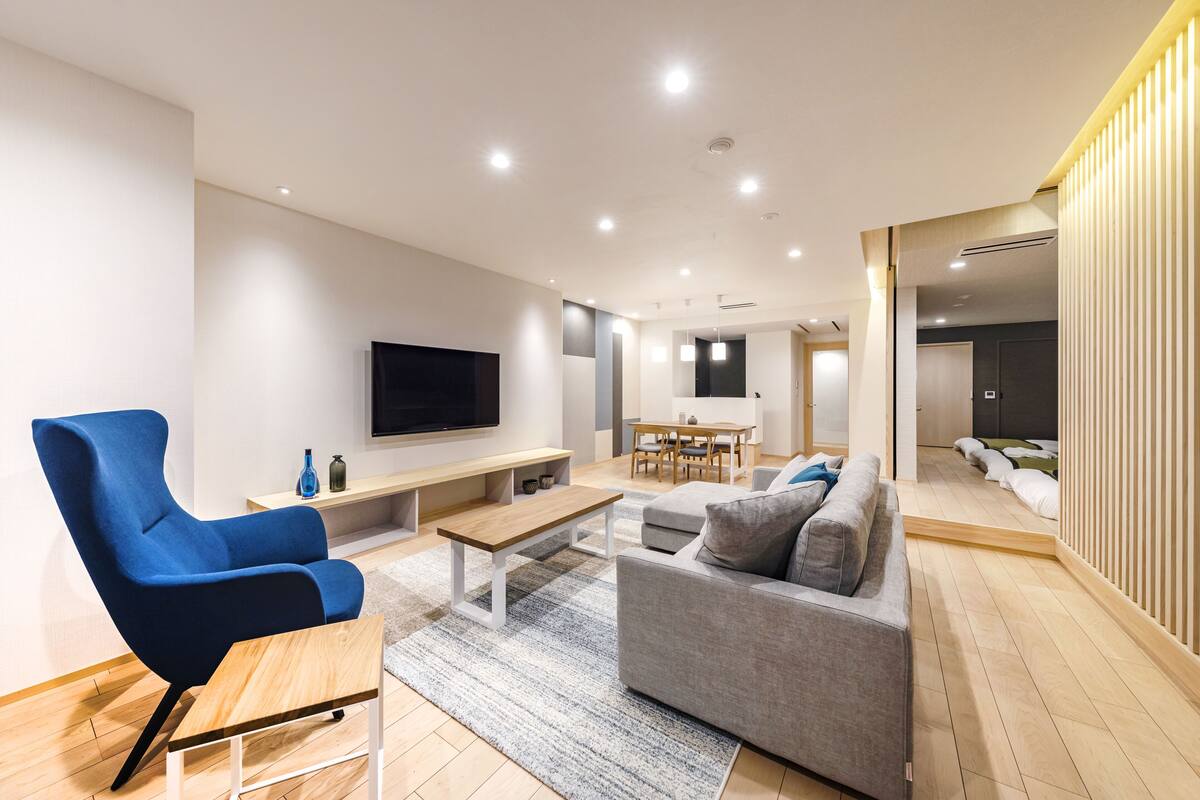 A modern living room with a blue armchair, grey sofa, wooden coffee table, and a flat-screen TV mounted on the wall.