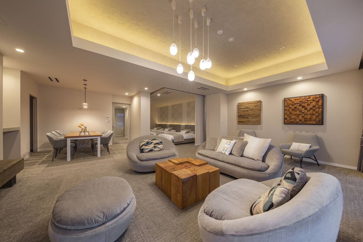 A modern living room with a dining area, grey sofas, a wooden coffee table, and a ceiling light fixture.