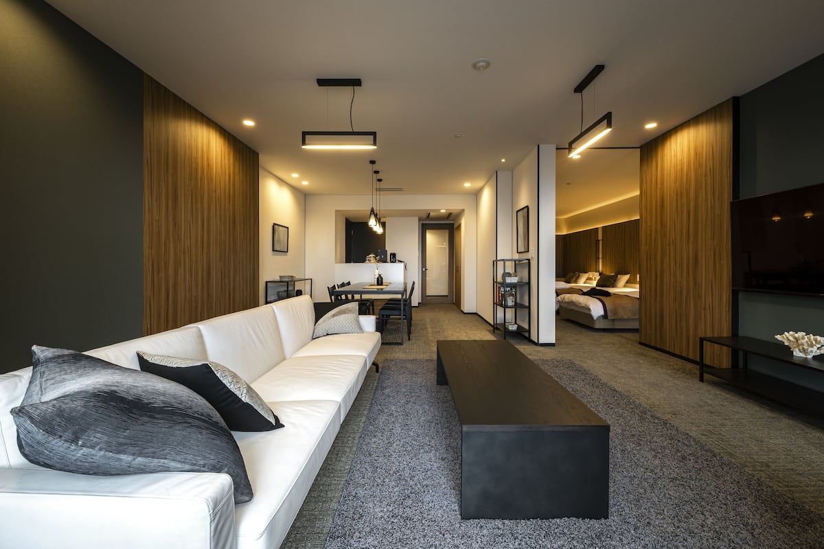 A modern living room with a white sofa, black and gray pillows, a dark coffee table, and a TV on the right.