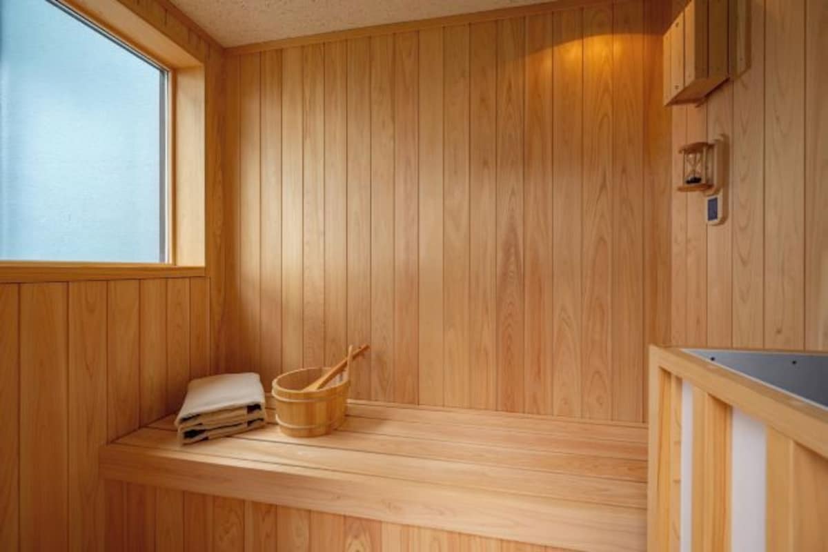 A wooden sauna with a bench, a window, and a small shelf with towels and a wooden bucket.