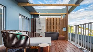 Una terraza de madera con un sofá, una mesita y una bañera grande.
