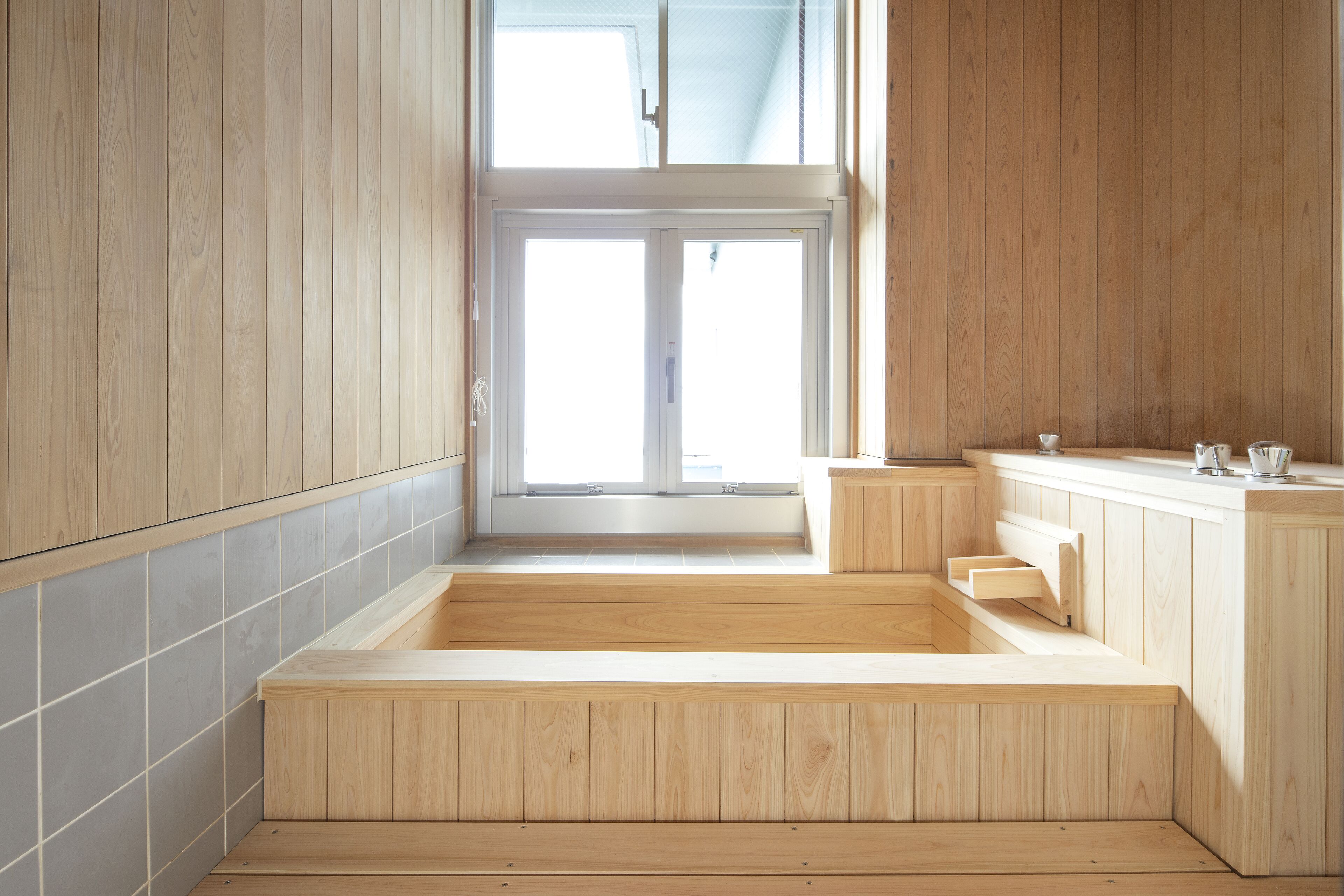 A modern bathroom with wooden cabinetry, a large bathtub, and a window providing natural light.