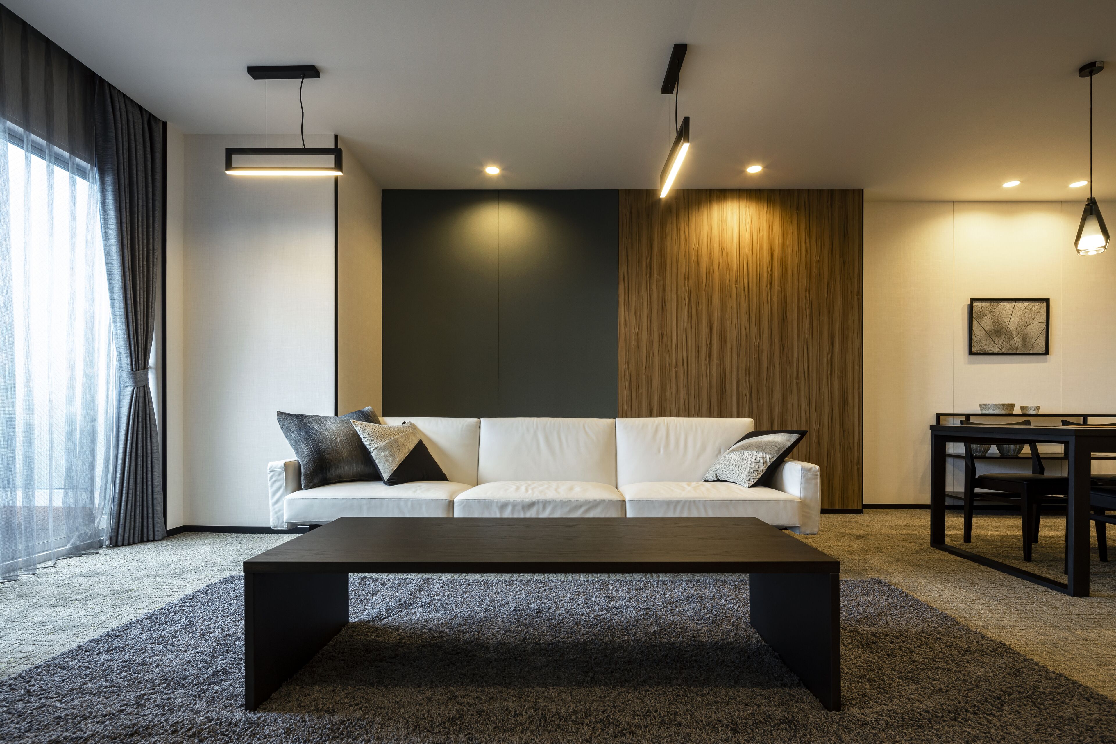 A modern living room with a white sofa, a dark coffee table, and a dining area with a wooden accent wall.