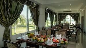A dining area with tables set for a meal, large windows with curtains, and a view of a landscaped area. - Gassan Panorama Golf Club (Ban Thi)