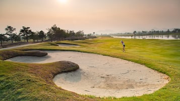 A golf course with sand bunkers, a water body, and trees in the background.