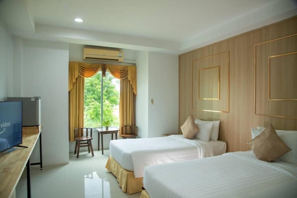 Habitación de hotel con dos camas, un escritorio con televisor, una ventana con cortinas y vistas al exterior.