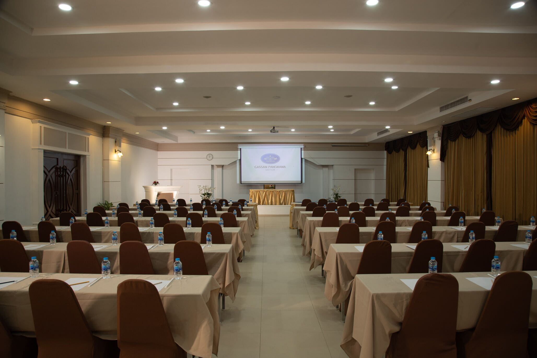 A conference room with rows of tables, chairs, and a projection screen displaying "CASSAN PANORAMA".