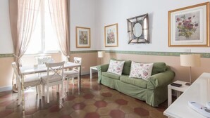A room with a green sofa, white chairs, a dining table, and a radiator. - Romantico by Interhome (Rome: Historical City Center)