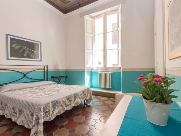 A bedroom with a bed, a window, a radiator, a potted plant, and a painting on the wall. - Romantico by Interhome (Rome: Historical City Center)