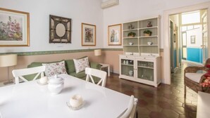 A room with a dining table, chairs, a sofa, a cabinet with glass doors, and a hallway leading to a balcony. - Romantico by Interhome (Rome: Historical City Center)