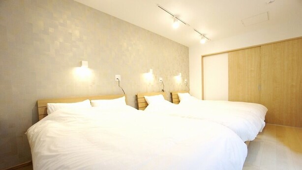 A hotel room with two beds, a wooden wardrobe, and wall-mounted lighting. - Sakura 612 (Sapporo)
