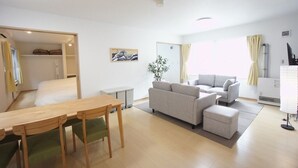 A modern, well-lit living room with a wooden dining table, grey sofas, and a small side table. - Sakura 612 (Sapporo)