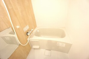 Eine kleine, weiße Badewanne mit Duschkopf und Bedienfeld neben einer Holztür.