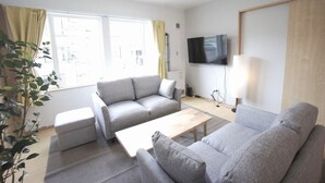 A modern living room with a grey sofa set, a wooden coffee table, and a flat-screen TV mounted on the wall. - Sakura 612 (Sapporo)