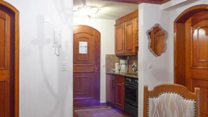 Un couloir étroit mène à une cuisine équipée de meubles en bois, d’une machine à café et d’une cuisinière.