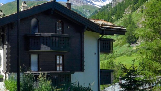 Un chalet traditionnel doté d’un balcon, situé au pied d’un sommet montagneux.