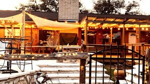 An outdoor seating area with tables and chairs, a covered patio, and a decorative fence with lights. - Cody's Happy Trails Ranch Vacation Rental -New Braunfels Texas! (New Braunfels)