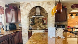 A kitchen with a stone arch, dark wooden cabinets, a marble countertop, and a black leather bar stool. - Cody's Happy Trails Ranch Vacation Rental -New Braunfels Texas! (New Braunfels)
