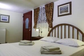 A neatly made bed with white linens and two pillows, a wooden headboard, a bedside table with a lamp, a door with a window, and a framed picture on the wall. - Galaxidi Mansion, Private villa (Galaxidi)