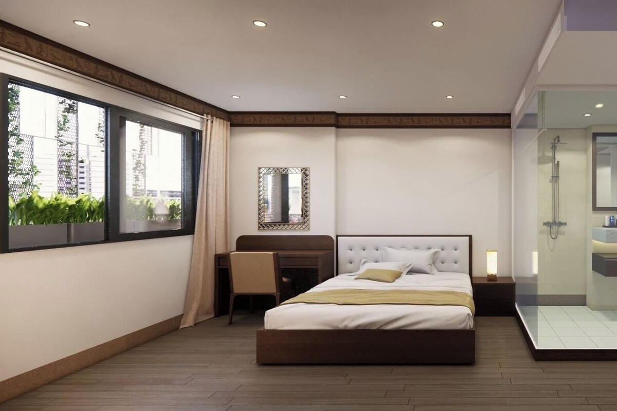 Quarto de hotel moderno com uma cama grande, escrivaninha, banheiro com box de vidro e vista para a cidade.