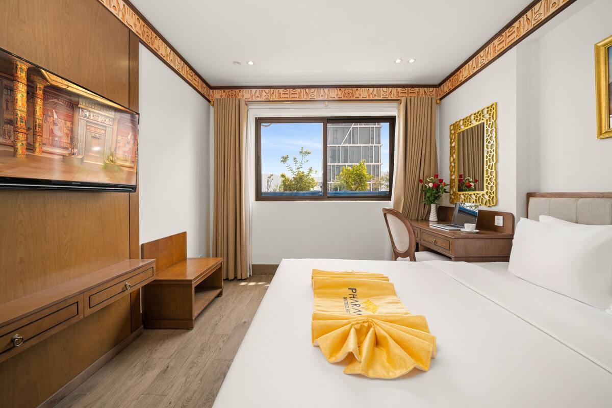 Hotelkamer met een groot bed, een bureau, een stoel, een televisie en een raam met uitzicht op gebouwen en bomen.