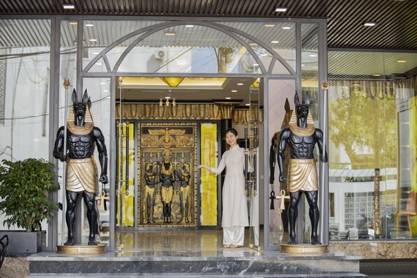 A hotel entrance with two statues of Egyptian figures, a woman in traditional attire, and a golden door.
