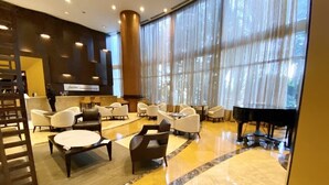 A spacious lobby with a grand piano, comfortable seating, and large windows offering a view of the outdoors. - Ocean View Suite at T. International STR-02496 (Sunny Isles)