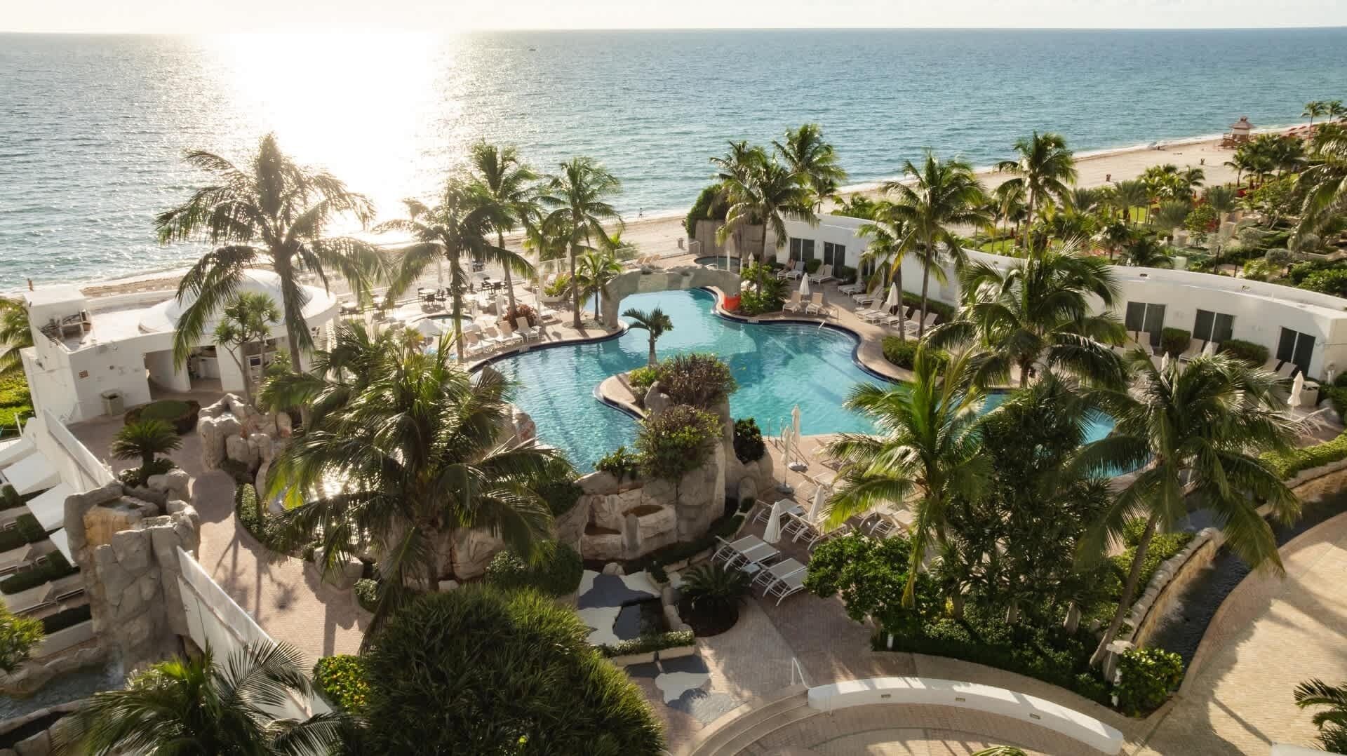 Un resort con piscina centrale, palme e vista sulla spiaggia.
