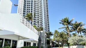 A modern hotel with a curved facade, outdoor seating area, and palm trees. - Ocean View Suite at T. International STR-02496 (Sunny Isles)