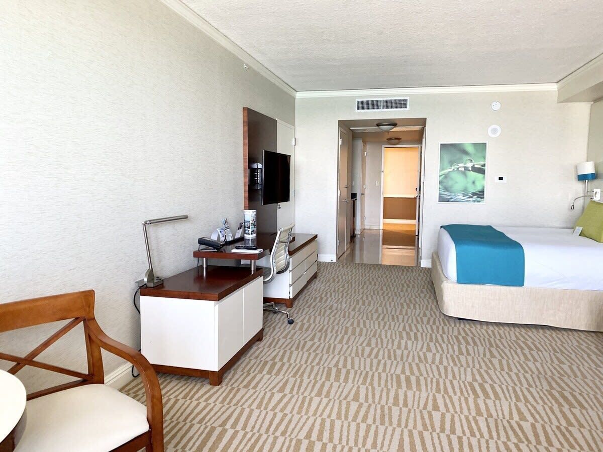 A hotel room with a desk, chair, bed, and a TV.