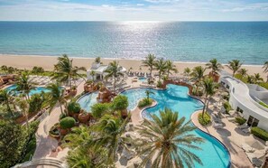 Een resort met meerdere zwembaden, palmbomen en uitzicht op het strand.