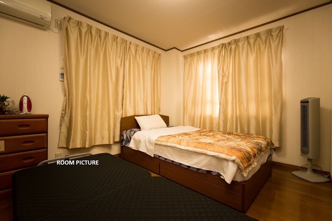 Ein Schlafzimmer mit einem Einzelbett, einem Schminktisch, einer Klimaanlage und einem Standventilator.
