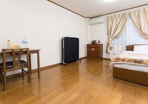 Ein Schlafzimmer mit Holzboden, einem Bett mit floralem Überwurf, einem Schreibtisch mit Stuhl, einer kleinen Kommode und einem schwarzen Heizkörper.