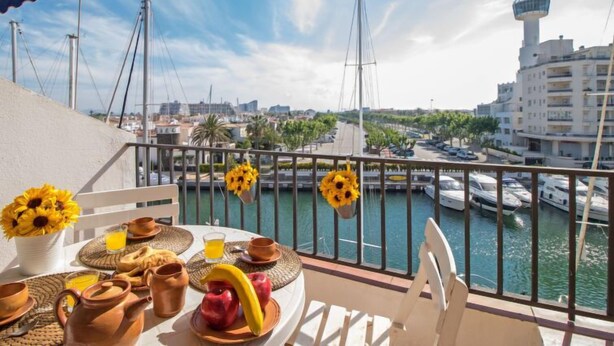A balcony with a table set for breakfast, overlooking a marina with boats and a cityscape. - Caballito de Mar by Interhome (Empuriabrava)