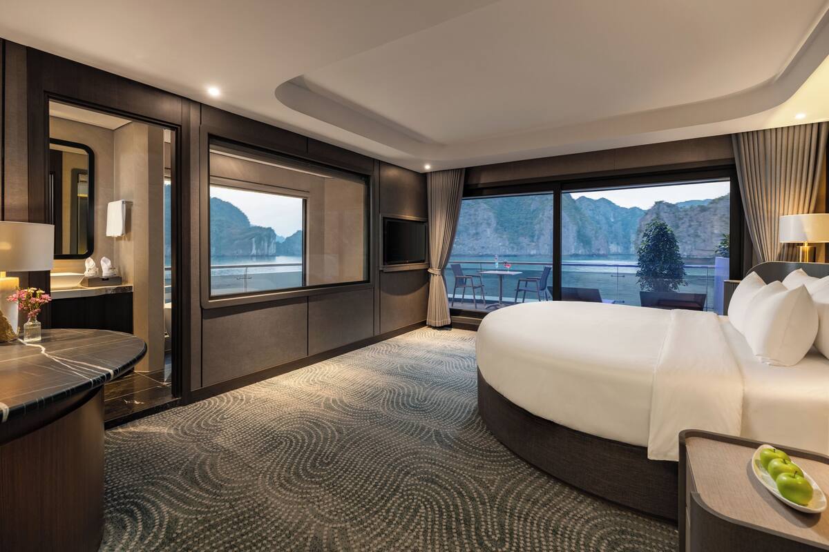 A modern hotel room with a large bed, a desk, a TV, and a view of the mountains.