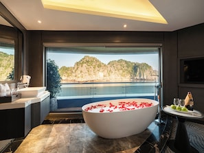 Une salle de bain moderne avec une grande baignoire, un lavabo et une vue sur un plan d’eau et des montagnes.