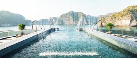 Una piscina con una cascada, rodeada por una terraza de piedra y plantas en macetas.