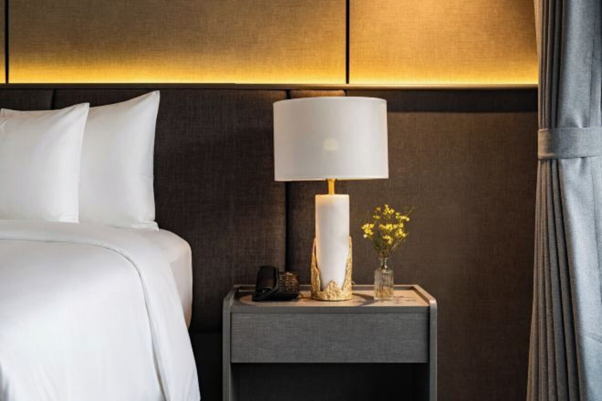 Una habitación de hotel con una cama, una mesita de noche con lámpara y un jarrón con flores.