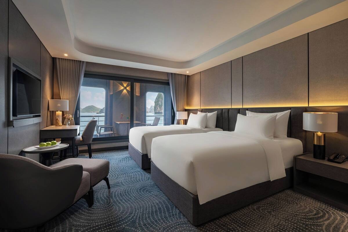 A modern hotel room with two beds, a desk, a chair, and a TV.