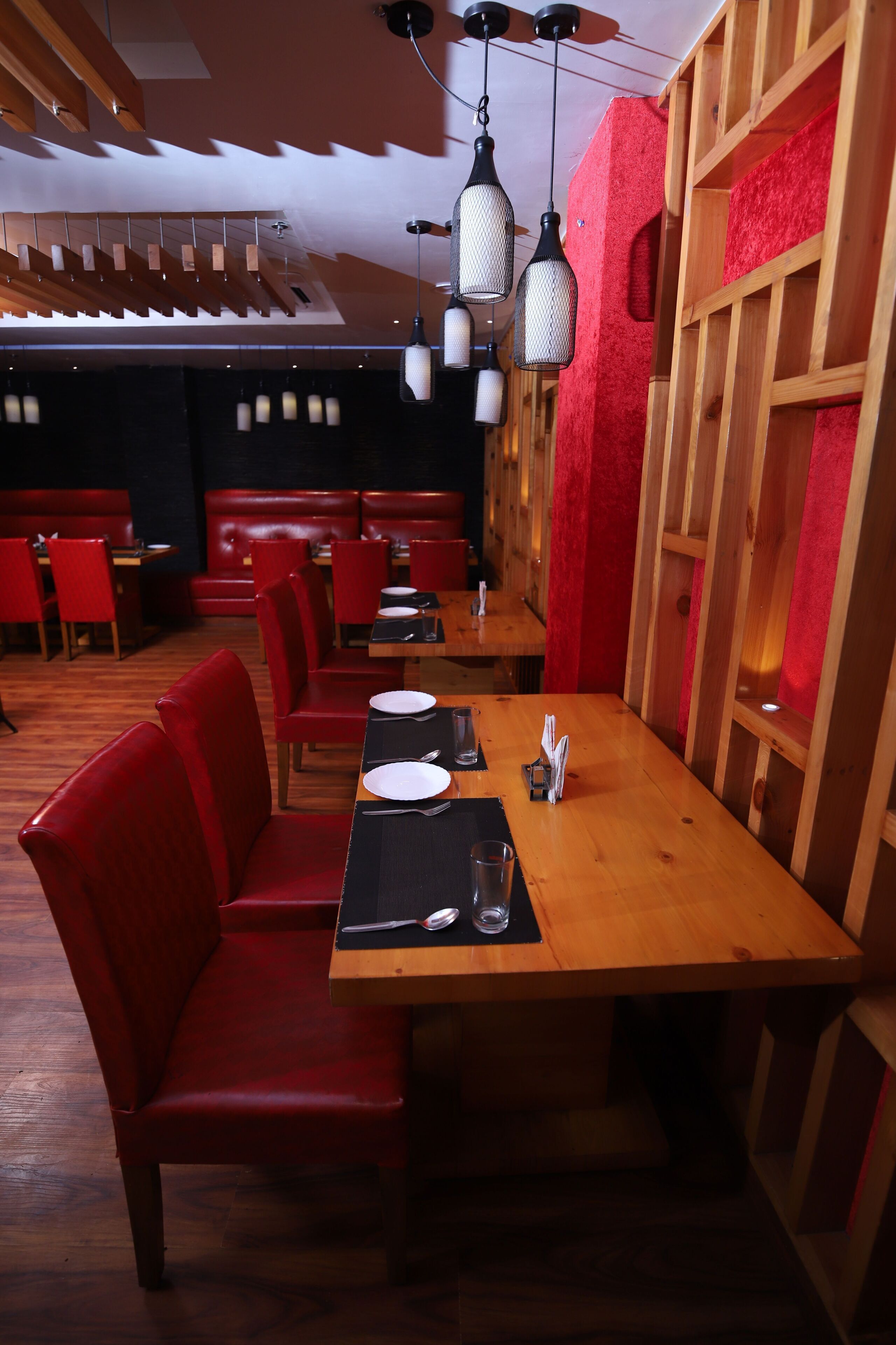 A restaurant interior with wooden tables, red upholstered booths, and hanging pendant lights.