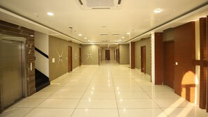 A hotel corridor with a shiny tiled floor, wooden doors, and a ceiling with recessed lighting. - Hotel Visit (Barnala)