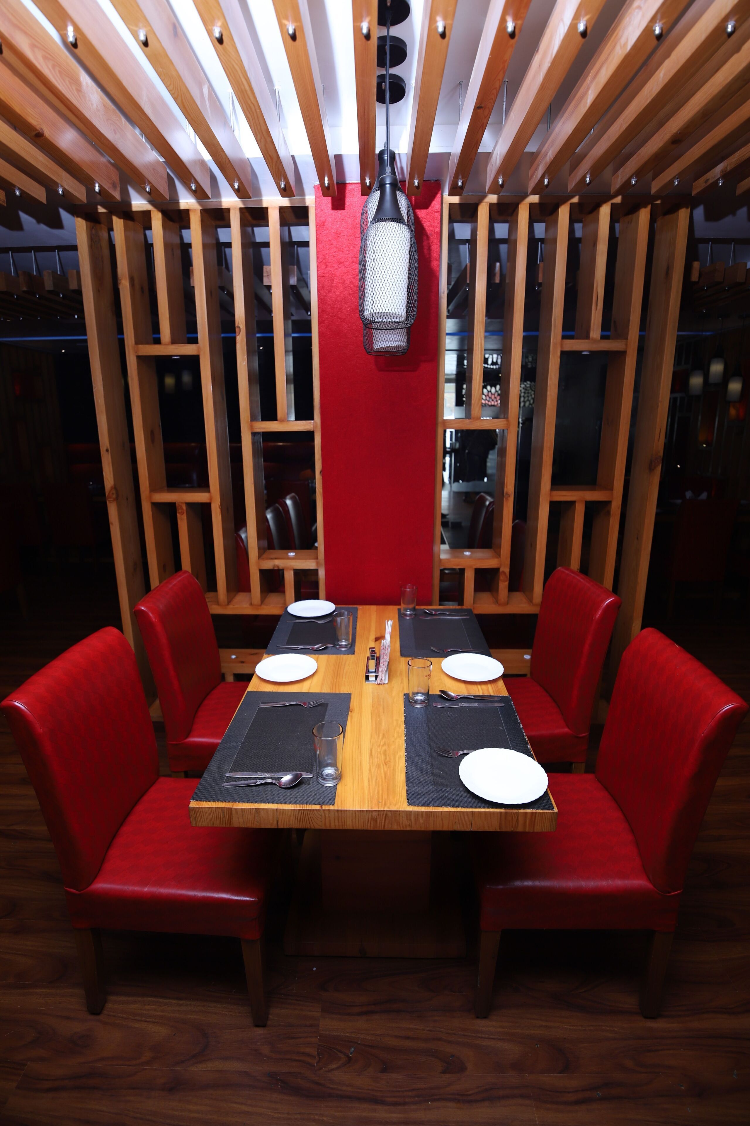 Un comedor con mesa de madera, sillas tapizadas en rojo y una pared decorativa roja.